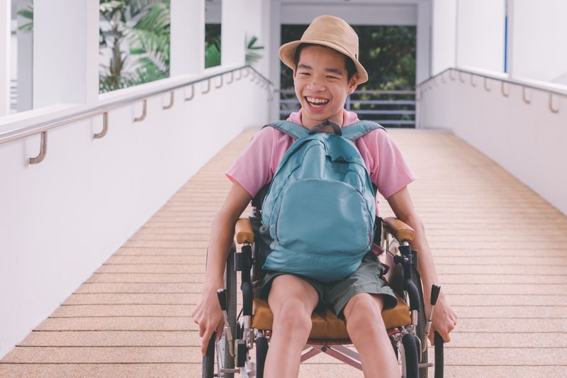 A smiling teen in a wheelchair rolls down a ramp.