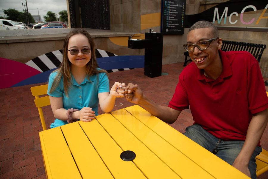 A young woman with Down syndrome and a young man share a fist bump at a cafe table.